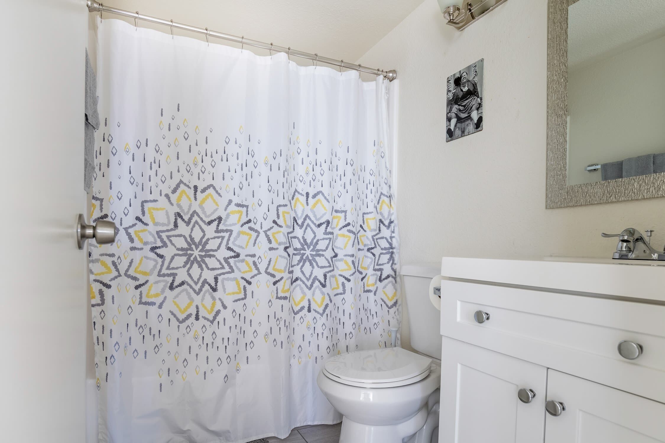 Een badkamer met douchegordijn met een geometrisch patroon, een toilet en een witte wastafel met spiegel.