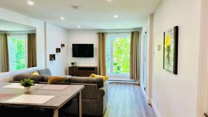 Una sala de estar moderna con un sofá, un televisor, una mesa de comedor y ventanas grandes.
