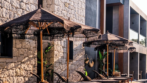 A pool area with lounge chairs and umbrellas, stone walls, and a modern building in the background. - The Grey Alaçatı (Cesme)
