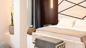 Ein modernes Hotelzimmer mit einem großen Bett, einem Nachttisch, einer Topfpflanze und Blick ins Freie.
