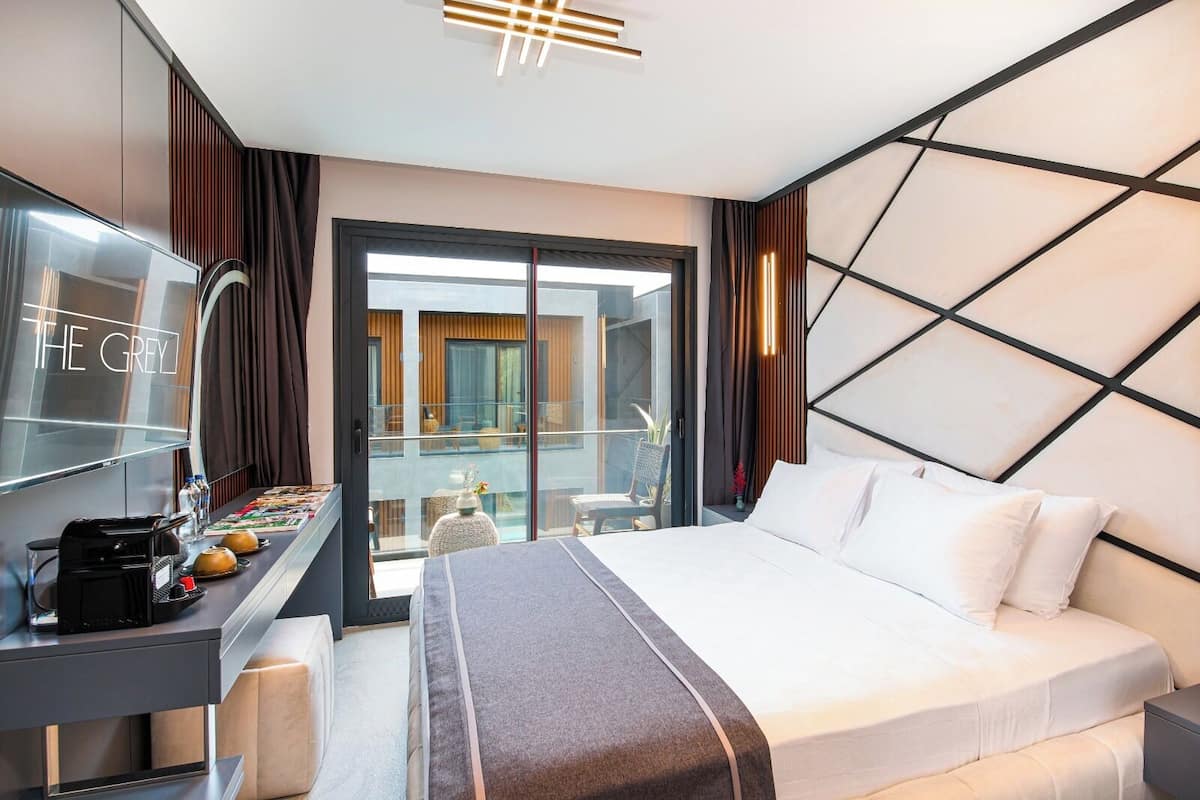Una moderna camera d'albergo con un letto grande, una scrivania con una macchina per il caffè, una TV e un balcone con vista sulla città.