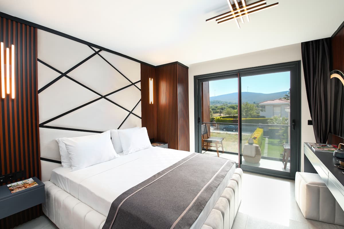 Una camera d'albergo moderna con un letto grande, una scrivania con una sedia e un balcone vista campagna.