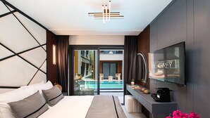 A modern hotel room with a bed, a TV, a console table, and a view of an outdoor swimming pool. - The Grey Alaçatı (Cesme)