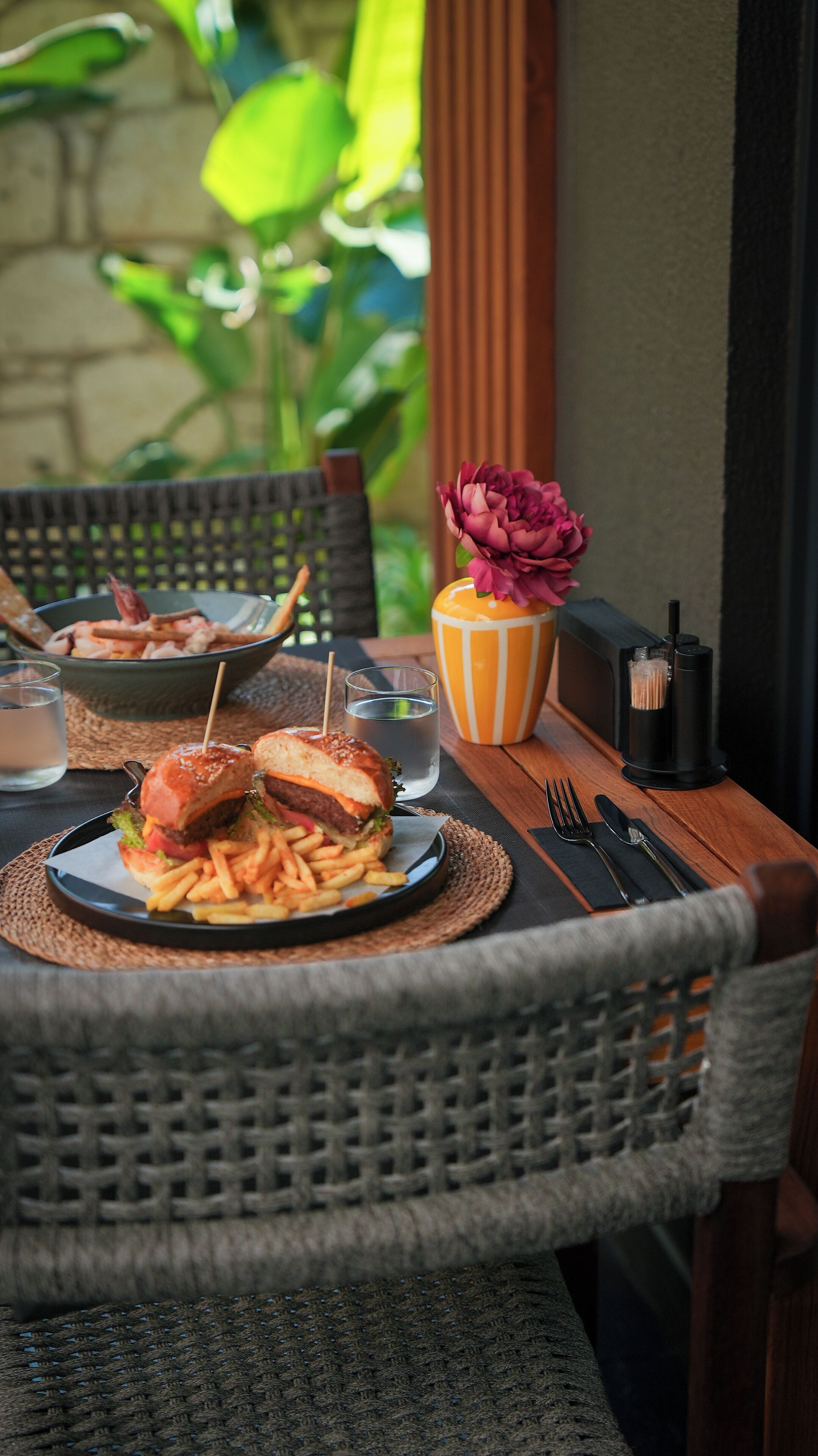A dining table with a plate of food, a glass of water, and a striped vase with a flower.