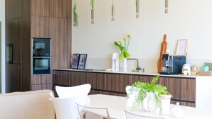 A modern kitchen with built-in appliances, a dining area with white chairs, and hanging plants. - Magnificent sea view flat Les Sables - 7 pers (Les Sables-d´Olonne)
