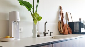 A kitchen with a white countertop, a white water dispenser, a white vase with a plant, a wooden guitar, and a coffee cup. - Magnificent sea view flat Les Sables - 7 pers (Les Sables-d´Olonne)
