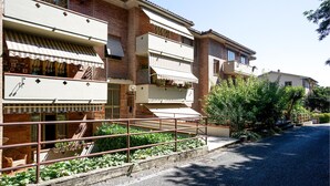 A row of multi-story residential buildings with balconies, a gravel driveway, and a metal fence. - Lovely apartment in Monteriggioni (Monteriggioni)