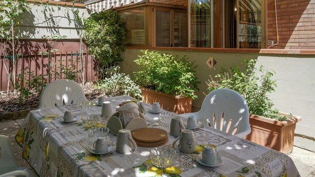 An outdoor dining area with a table set for four, surrounded by potted plants and a brick wall. - Lovely apartment in Monteriggioni (Monteriggioni)