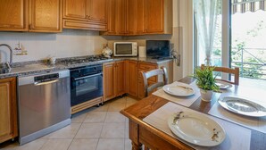 A kitchen with wooden cabinets, stainless steel appliances, a dining table with chairs, and a view of the outdoors. - Lovely apartment in Monteriggioni (Monteriggioni)