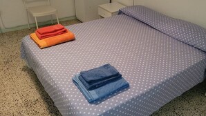 Ein Einzelbett mit Punkten, zwei gefaltete Handtücher, ein Nachttisch und ein Stuhl.