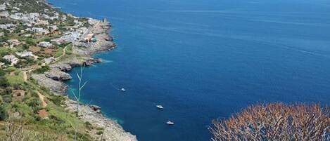 Un pueblo costero con acantilados rocosos, mar azul cristalino y barcos.