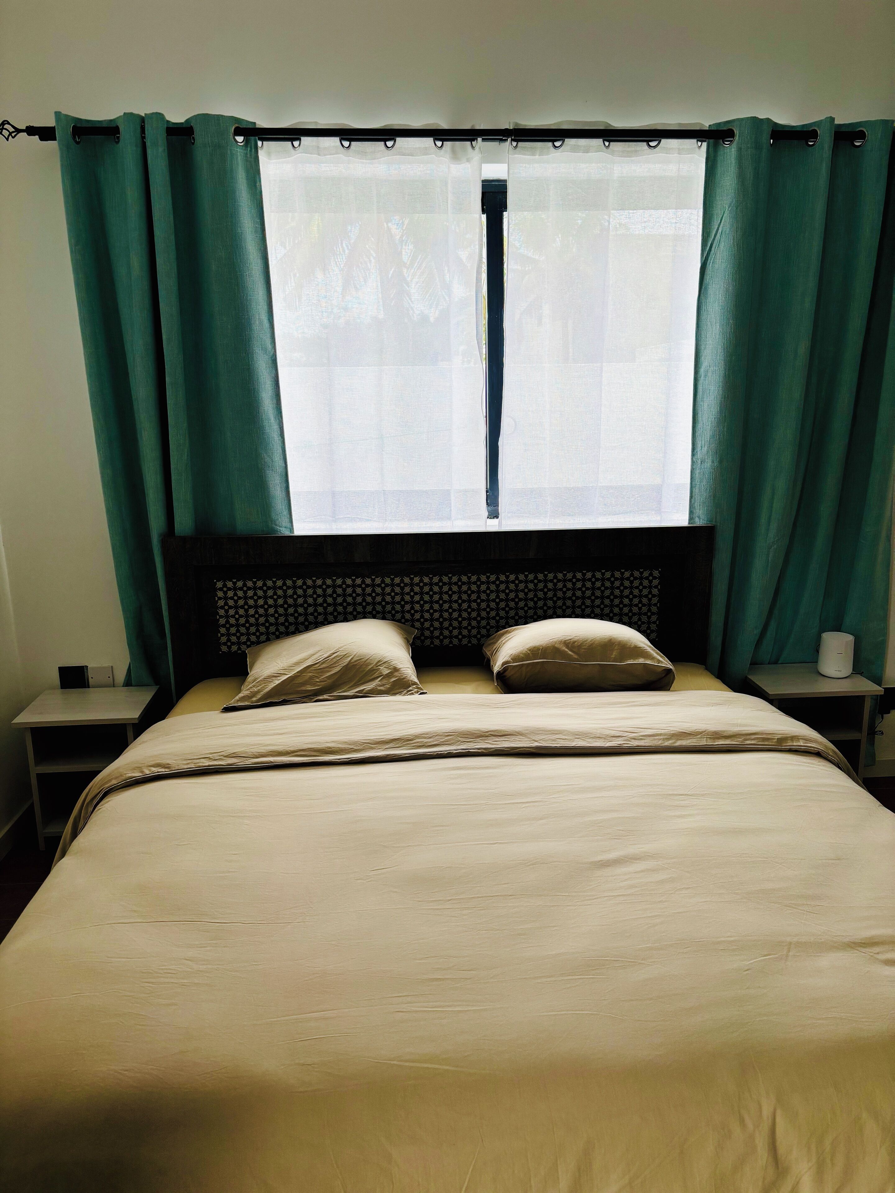 A bed with a headboard, two pillows, a bedside table, and a window with curtains.