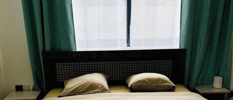 A bed with a headboard, two pillows, a bedside table, and a window with curtains.