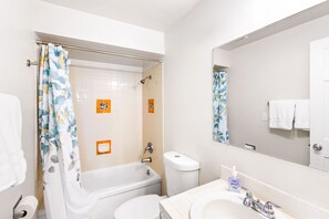 Bathroom features a bathtub, toilet, and sink, with a shower curtain and mirror above the sink.