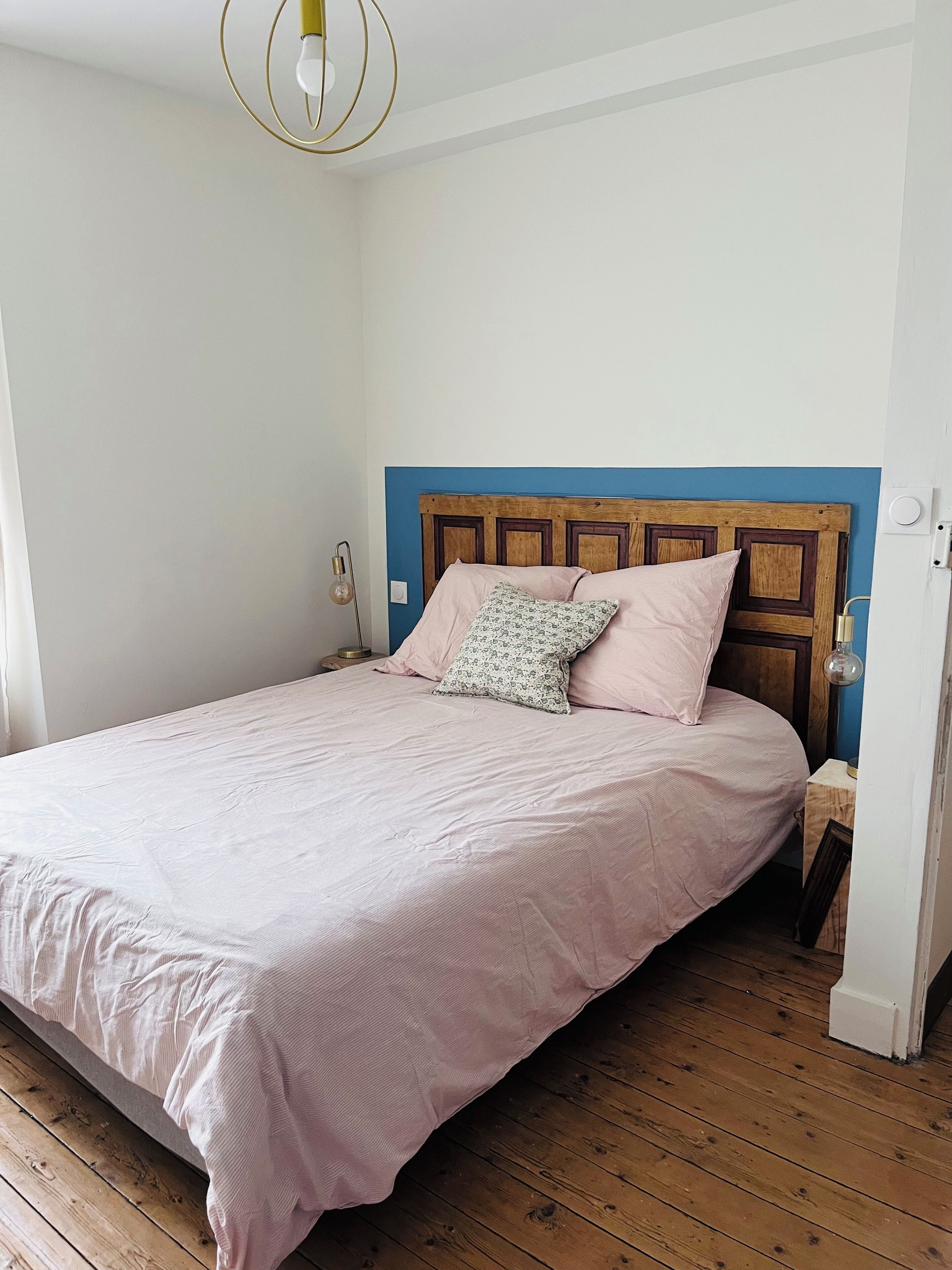 Une chambre avec une tête de lit en bois, un lit avec une literie rose et un plancher en bois.