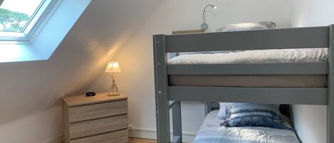 A bedroom with a bunk bed, a bedside table with a lamp, a wooden dresser, and a skylight.