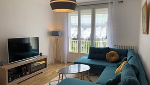 Uma sala de estar moderna com televisão de tela plana, um conjunto de sofás, uma mesa redonda pequena e um abajur.