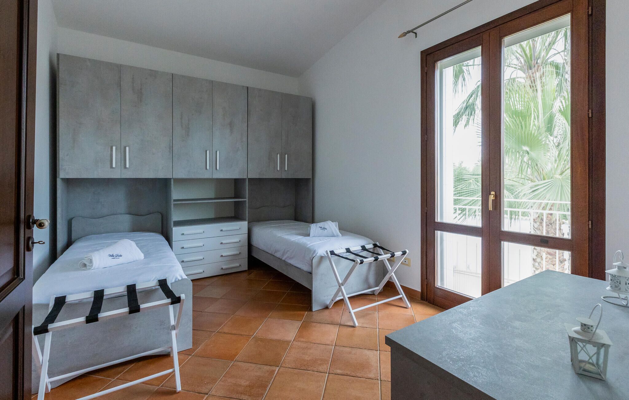 A bedroom with two beds, a wardrobe, a drying rack, and a window with a view of palm trees.