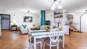 Amplia sala de estar con una mesa de comedor, sillas blancas, un sofá, una estantería y una escalera.