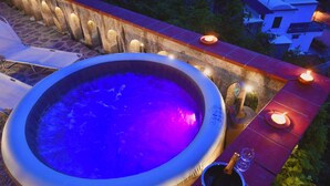 A hot tub with a blue light, a candle, and a bottle of champagne on a tiled patio.