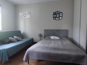 Een slaapkamer met een bed, een blauwe bank en een muur met ingelijste foto’s en een harttekening.