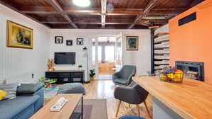 A cozy living room with a wooden ceiling, a TV, a fireplace, and a dining area with a table and chairs.