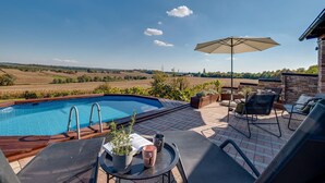 A poolside area with a view of the countryside, a table with a plant and a book, and outdoor seating.