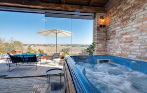 A hot tub area with a view of the countryside, a brick wall, and a glass door.