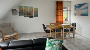 Un soggiorno moderno con un divano in pelle nera, un tavolo da pranzo in legno con sedie, una lampada da terra e vista sul mare attraverso una finestra.