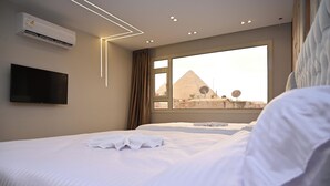 A hotel room with two beds, a flat-screen TV, an air conditioner, and a view of the pyramids. -  Pyramids Enigma Grand Lodge (Giza)
