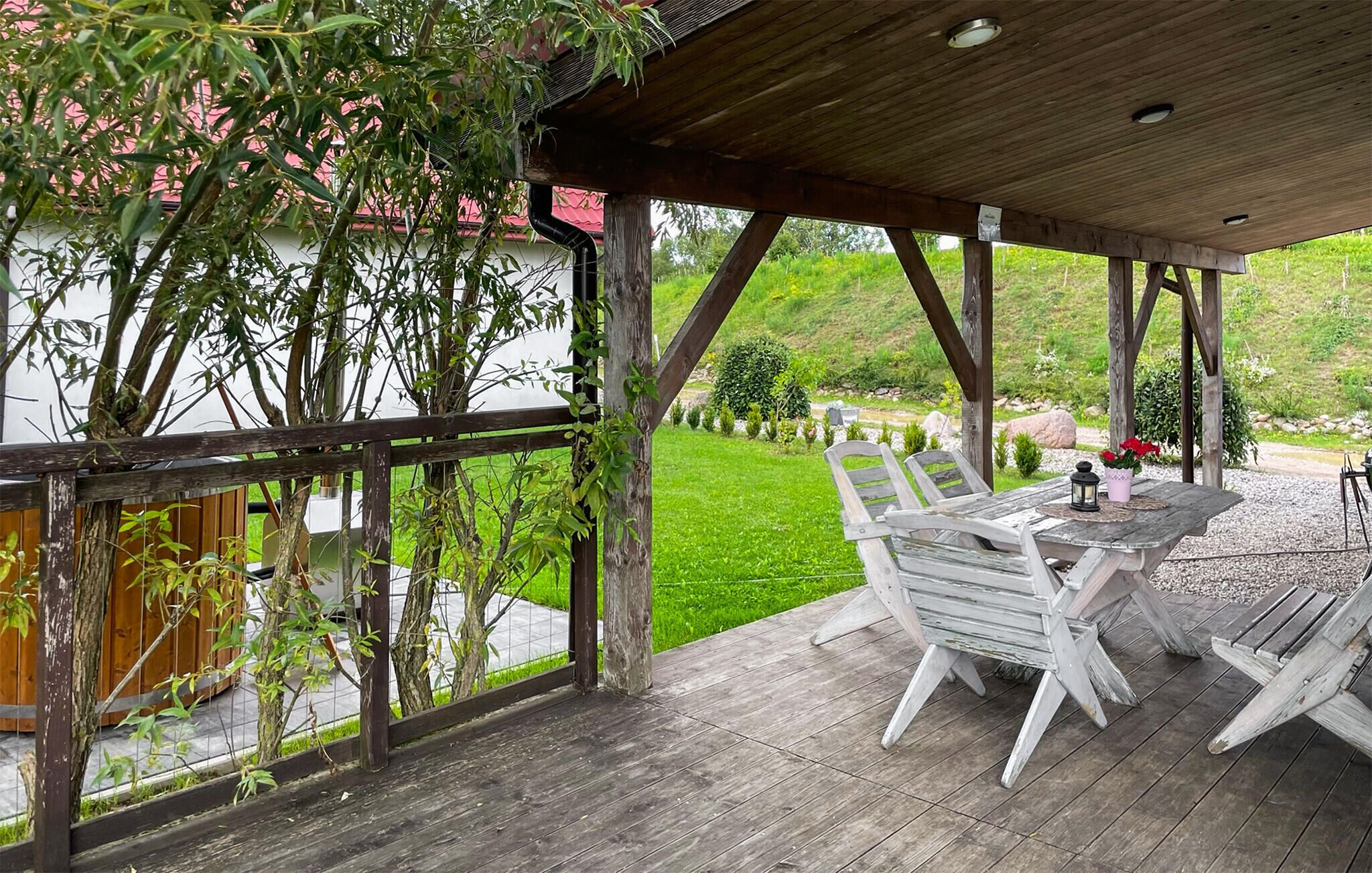 Una terraza de madera con una mesa y sillas, con vistas a una zona verde con árboles y un edificio rojo al fondo.