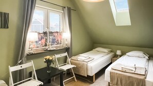 Ein kleiner, gemütlicher Raum mit einem Bett, einem Sessel, einem Tisch und einem fenster mit Vorhängen.