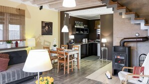 Ein modernes Wohnzimmer mit einer Couch, einem Esstisch und Stühlen, einer Küchenzeile mit Herd und einer Treppe, die eine weitere Ebene hinaufführt.