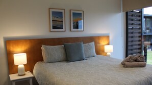 Un letto ben rifatto con una coperta a fantasia, due cuscini e un asciugamano arrotolato su un lato. Due abat-jour su comodini bianchi.