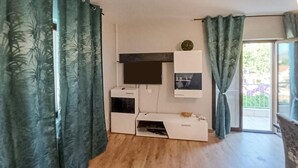 Une pièce dotée d’un téléviseur à écran plat fixé au mur, d’un petit meuble placé en dessous, et d’une porte coulissante donnant sur un espace extérieur.