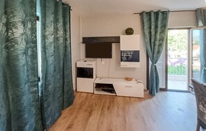 Une pièce dotée d’un téléviseur à écran plat fixé au mur, d’un petit meuble placé en dessous, et d’une porte coulissante donnant sur un espace extérieur.