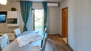 Une pièce comprenant une table à manger, des chaises, un téléviseur fixé au mur et une porte donnant sur l’extérieur.