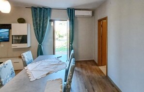 Une pièce comprenant une table à manger, des chaises, un téléviseur fixé au mur et une porte donnant sur l’extérieur.