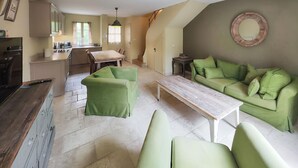 A living room with a green sofa set, a wooden coffee table, and a kitchen area with a sink and cabinets.