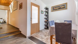 Une pièce avec un escalier en bois, un coin repas avec une table et des chaises, une bibliothèque et une horloge au mur.