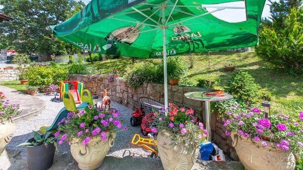 Un espace extérieur aménagé avec des sièges, un parasol vert, des plantes en pot et un mur en pierre.