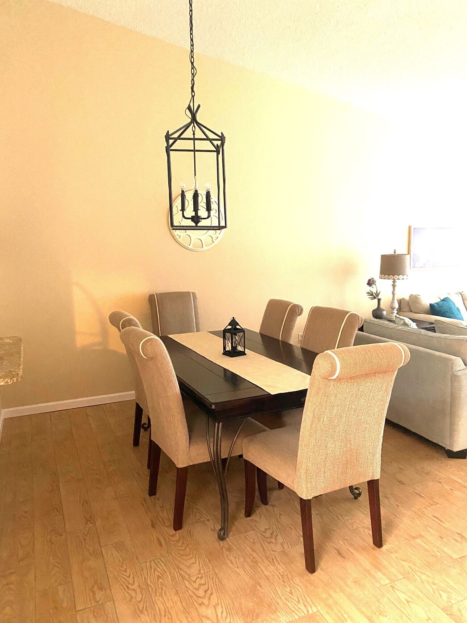 A dining area with a dark wooden table, six chairs, and a hanging lantern.