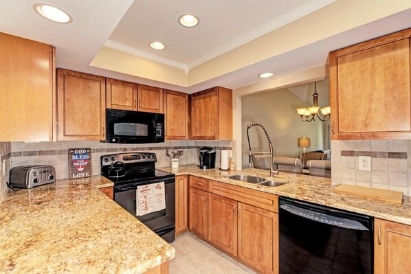 A kitchen with wooden cabinets, a black microwave, a stove, a sink, and granite countertops. - 5 MINUTES TO SIESTA KEY! PRIME LOCATION, STEPS TO THE POOL, COMPLETELY UPDATED! (Sarasota)