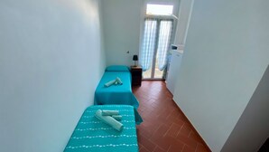 Un couloir étroit avec deux lits simples, chacun recouvert d’une courtepointe turquoise ornée de motifs en forme de cœur blancs.
