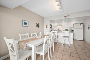 A modern kitchen with white cabinets, a dining area with white chairs, and a tiled floor.