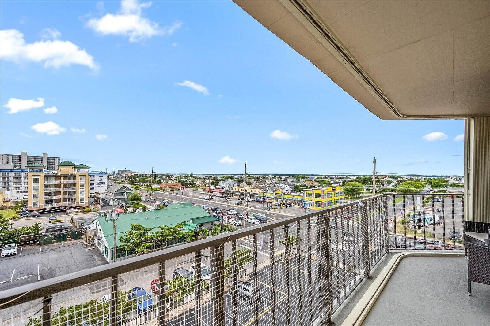 A balcony with a view of a cityscape, including buildings and a parking lot.