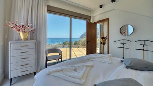 Een slaapkamer met een groot bed, een dressoir, een stoel en uitzicht op zee.