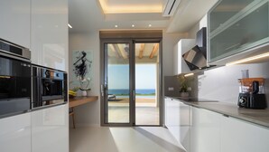 Een moderne keuken met inbouwapparatuur, uitzicht op zee en een minimalistisch design.