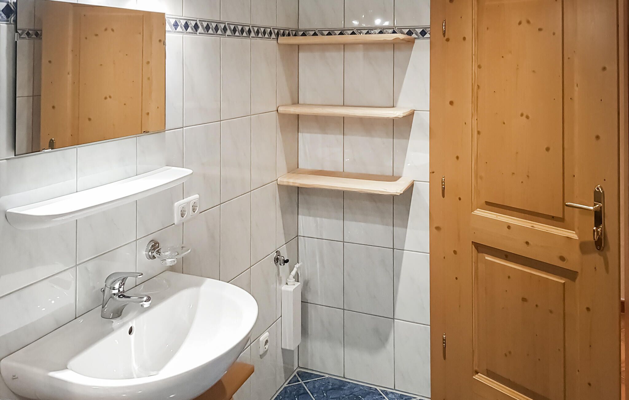 A bathroom with a white sink, mirror, and two wooden shelves.