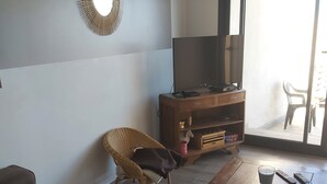 Ein Wohnzimmer mit einer Couch, einem Couchtisch, einem Korbstuhl, einem Fernsehschrank und einer Glasschiebetür, die zu einem Außenbereich führt.